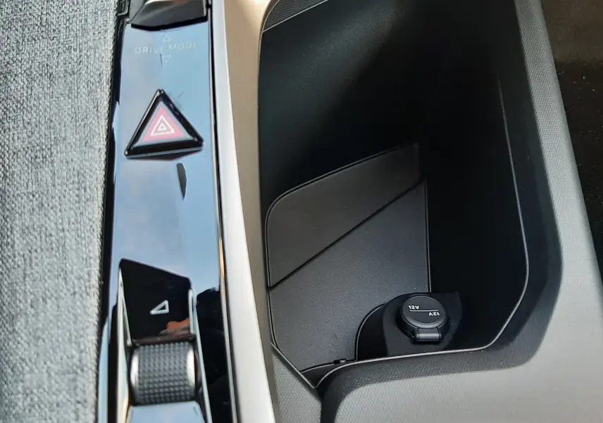Gros plan sur la console centrale noire et grise du Peugeot 5008 2025, avec commandes Drive Mode et prise 12V visible.