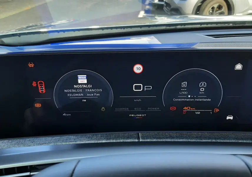 Tableau de bord numérique du Peugeot 5008 hybride 2025, affichage de la radio et consommation instantanée.
