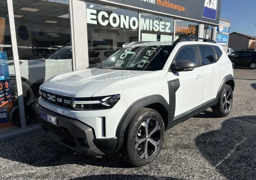 SUV Dacia Duster blanc métallisé en 3/4 avant droit, avec barres de toit noires et jantes alliage 18 pouces.