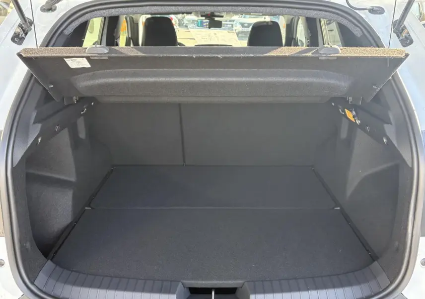 Coffre ouvert du Dacia Duster blanc métallisé 2024, vue arrière montrant l'espace de chargement vide et la tablette cache-bagages relevée.