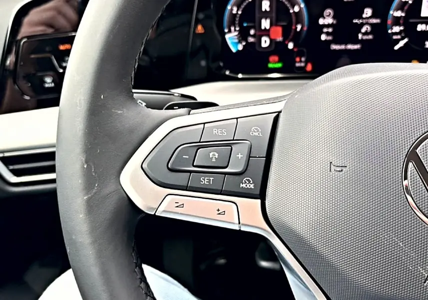 Gros plan sur le volant noir de la Volkswagen Golf 2026 avec commandes intégrées et tableau de bord numérique en arrière-plan.