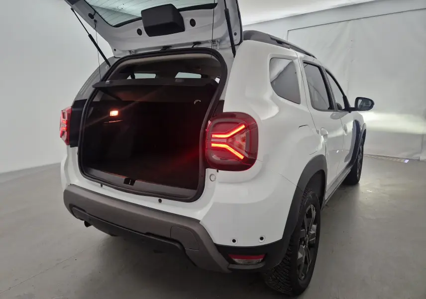 Vue arrière côté droit du Dacia Duster 4x4 blanc 2024 avec coffre ouvert et feux arrière allumés dans un studio.