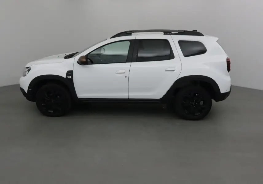 Profil côté gauche du Dacia Duster blanc 2024 avec jantes noires et barres de toit sombres, version 4x4 diesel.
