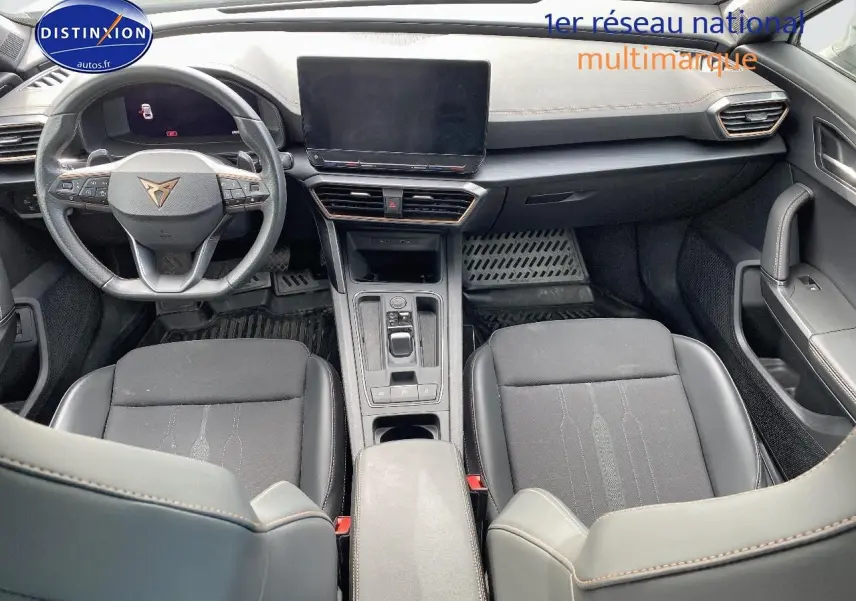 Vue intérieure avant du CUPRA Formentor 2023, sièges noirs tissu et similicuir, volant sport avec logo CUPRA, écran tactile central.