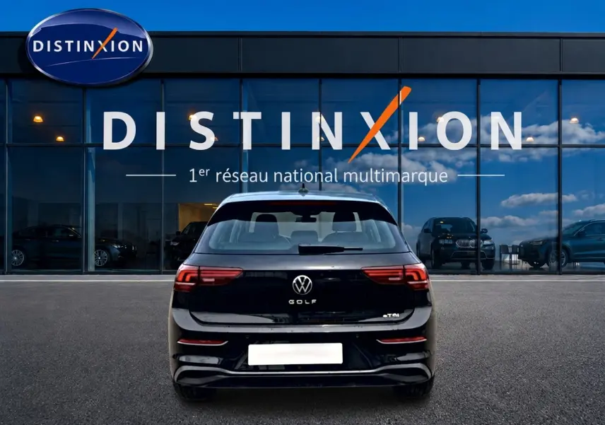 Vue arrière d'une Volkswagen Golf noire 2026 garée devant une vitrine avec logo Distinxion visible en arrière-plan.