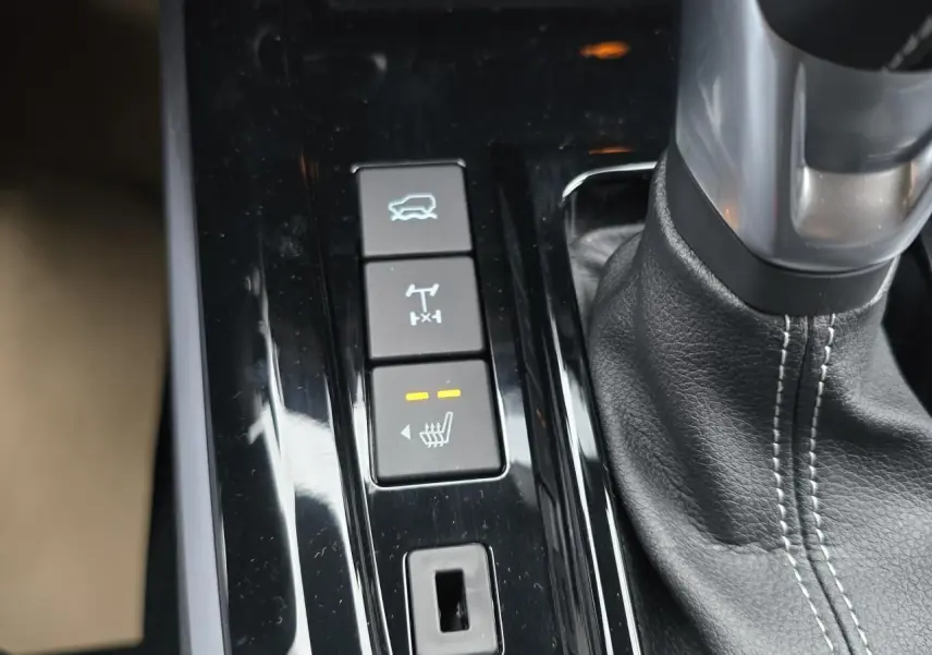 Gros plan sur la console centrale du pick-up Isuzu D-MAX orange, montrant levier de vitesse cuir et boutons de contrôle.