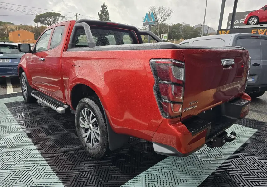 Vue 3/4 arrière droite d'un Isuzu D-MAX orange métallisé avec attelage et barre sport sur benne.