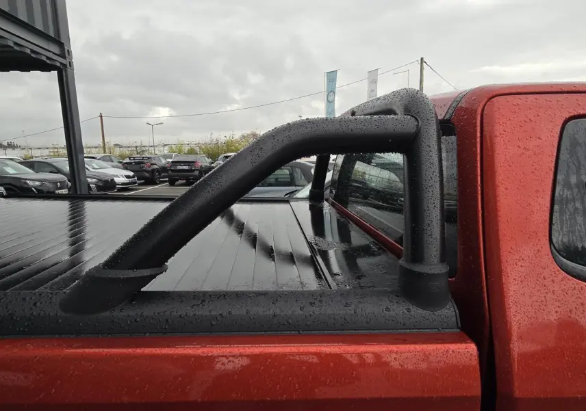 Vue latérale droite du pick-up Isuzu D-MAX orange métallisé avec sport bar noir et bac de benne fermé sous la pluie.