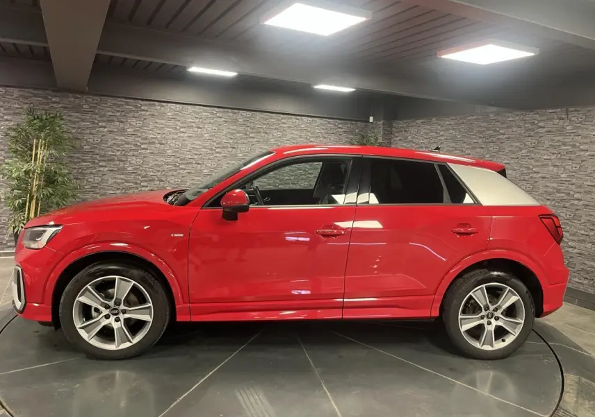 Audi Q2 S line rouge vue de profil côté gauche avec toit contrasté blanc et jantes sport 5 branches.