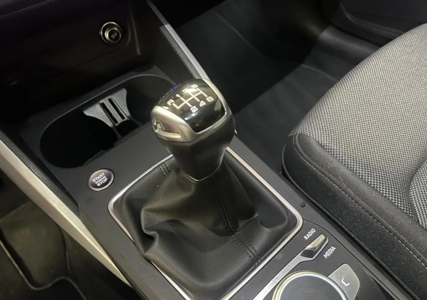 Le levier de vitesses manuel de l'Audi Q2 2024 en gros plan avec console noire et siège tissu gris.