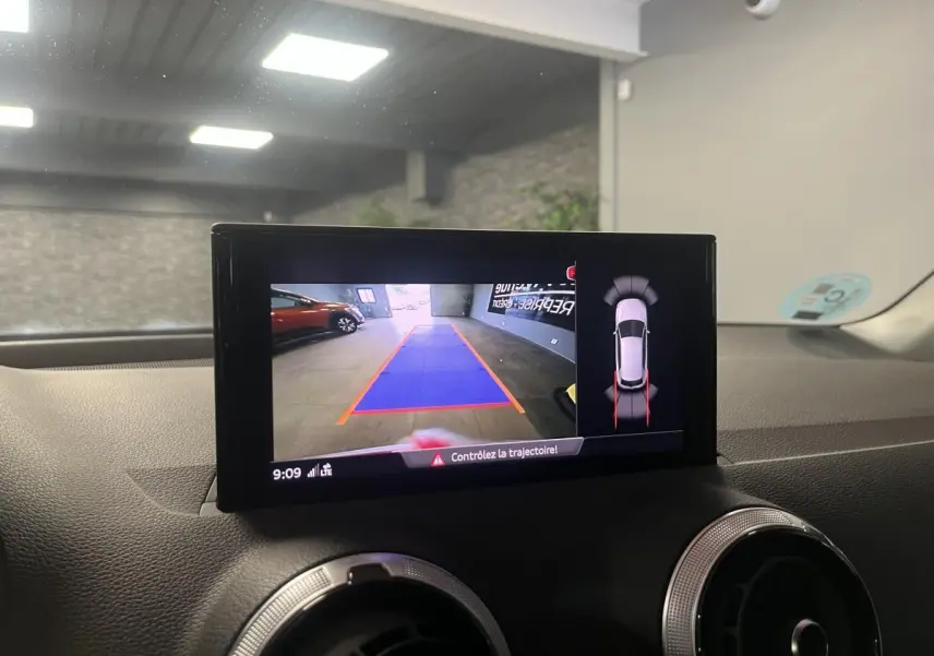 Écran intérieur affichant la caméra de recul et l'aide au stationnement du tableau de bord d'un Audi Q2 rouge.