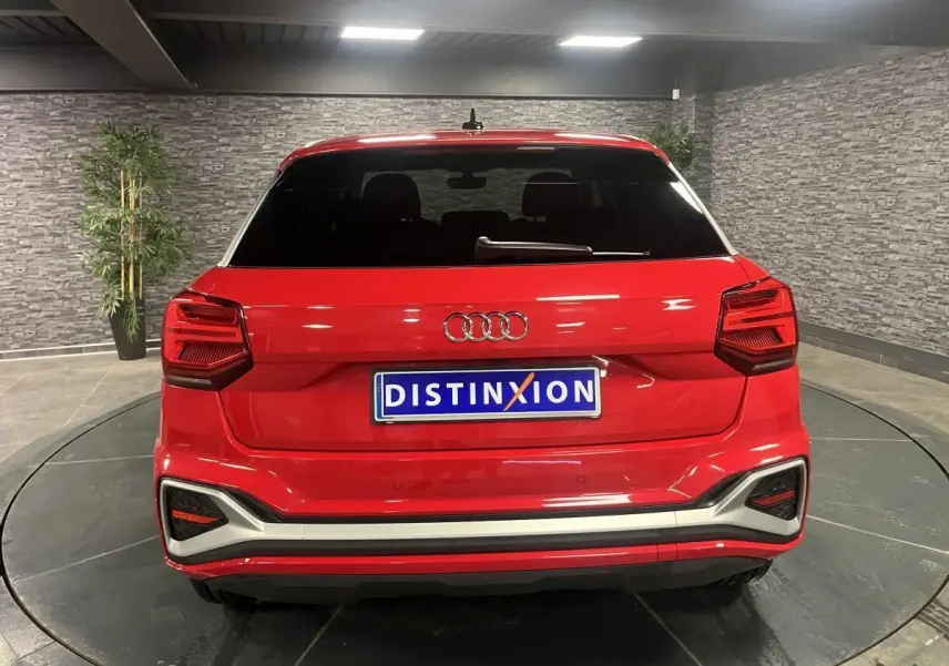 Vue arrière d'un Audi Q2 rouge 2024 avec hayon électrique et feux arrière LED dans un showroom.