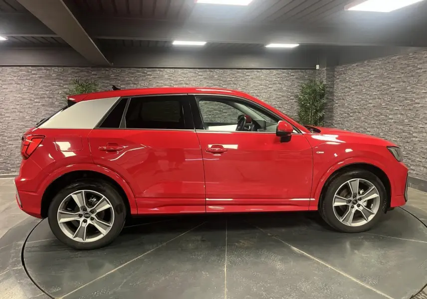 Profil côté gauche d'un Audi Q2 rouge 2024 avec jantes sport 5 branches et toit contrasté gris clair.