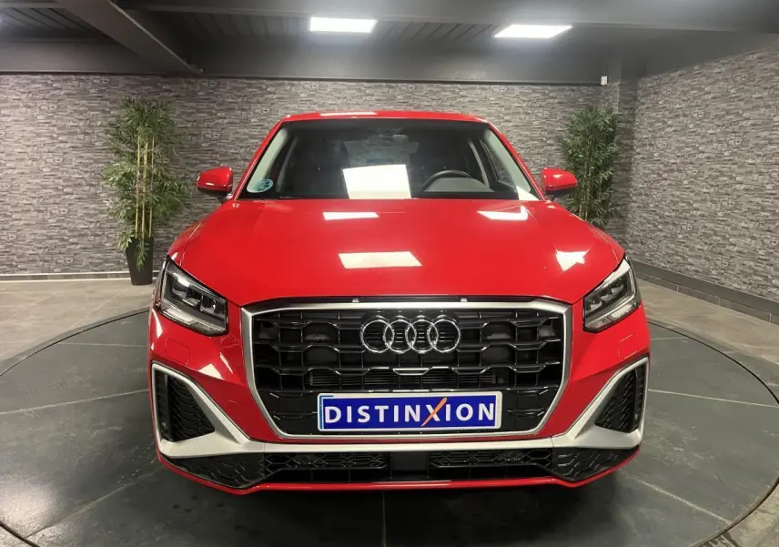 Vue frontale d'un Audi Q2 rouge S line 2024 avec calandre noire et détails argentés en intérieur showroom.