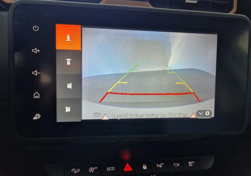 Écran central montrant la caméra de recul du Dacia Duster blanc 2024 avec lignes de guidage colorées.