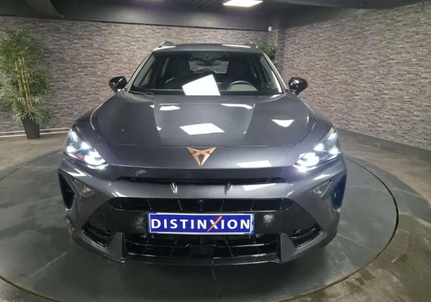 Vue avant d'une CUPRA Formentor gris métallisé avec feux allumés et logo cuivre sur le capot dans un showroom.