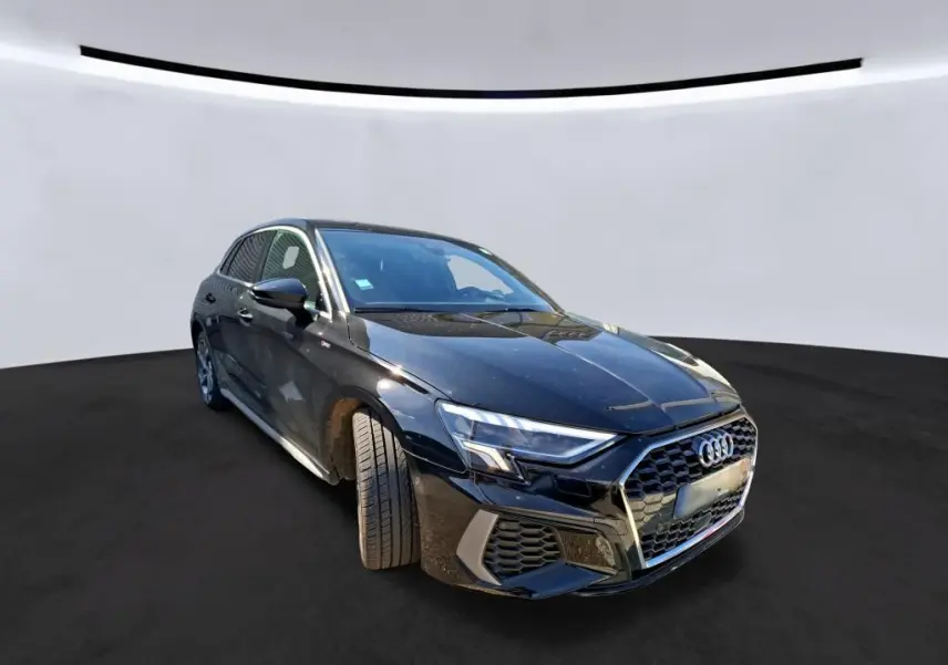 Vue de face d'une Audi A3 Sportback noire 2023 avec calandre hexagonale et phares LED, en intérieur showroom.