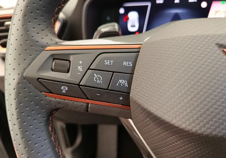 Gros plan sur la partie gauche du volant en cuir perforé noir avec surpiqûres orange de la CUPRA Leon ST 2024.
