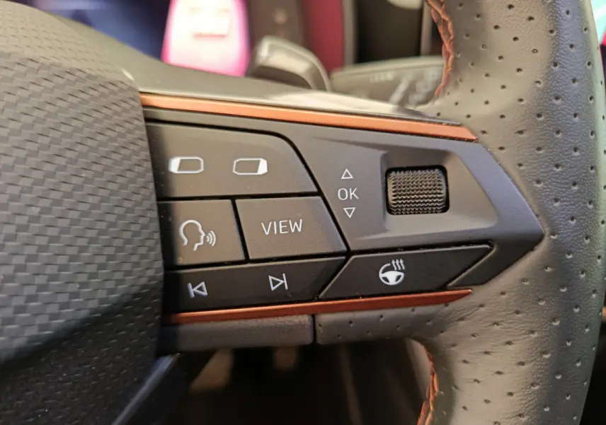 Gros plan sur les commandes gauche du volant perforé du CUPRA LEON ST gris foncé, avec boutons multifonctions et molette.