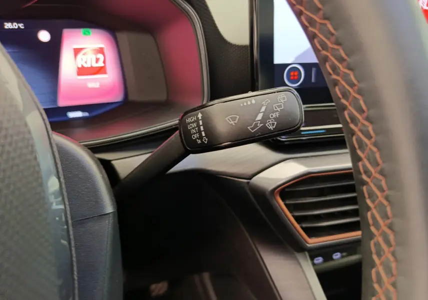 Gros plan sur la commande d’essuie-glace à gauche du volant cuir noir à surpiqûres orange du tableau de bord du CUPRA LEON ST 2024.