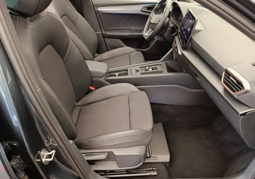 Intérieur côté conducteur de la CUPRA LEON ST gris foncé, sièges noirs avec surpiqûres orange et écran tactile central.