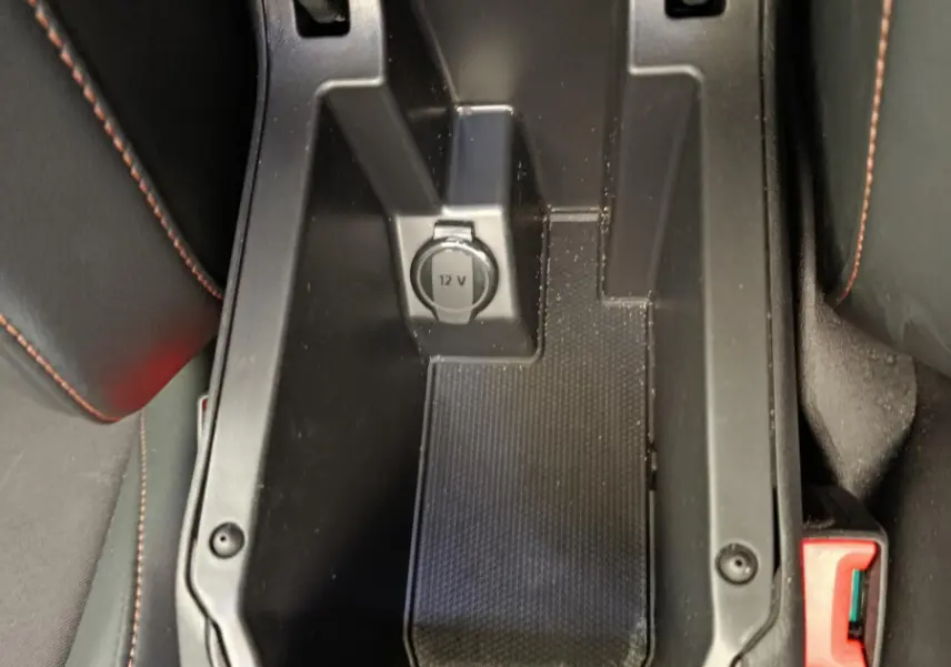 Vue plongeante sur le rangement central noir avec prise 12V et surpiqûres orange des sièges CUPRA LEON ST 2024.
