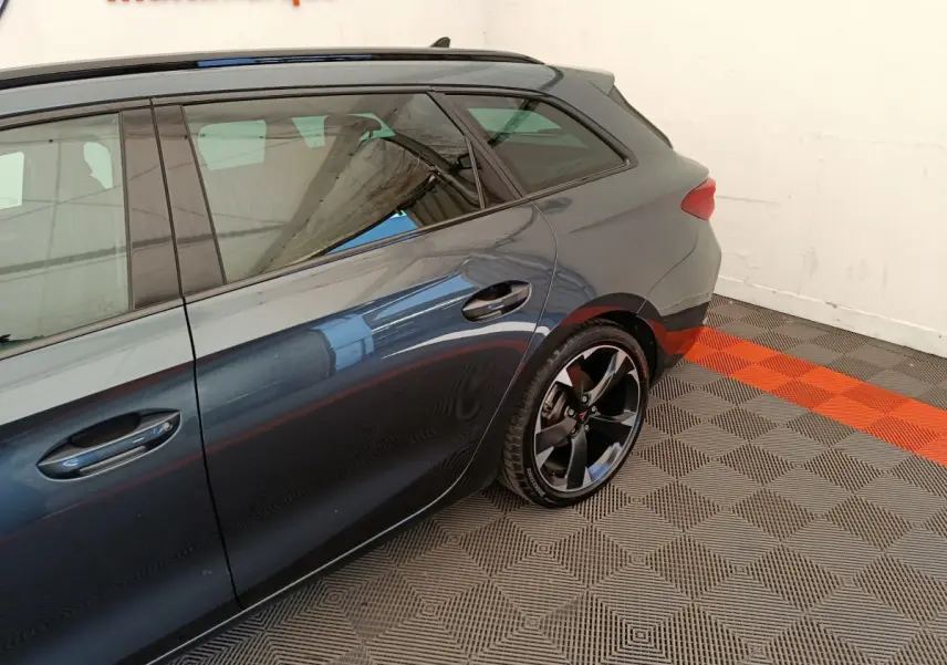 Vue latérale arrière droite d'une CUPRA LEON ST gris foncé avec jantes noires et poignées de porte intégrées.