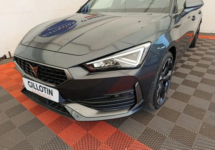 Vue 3/4 avant droit d'une CUPRA LEON ST gris foncé avec calandre noire et phares LED anguleux.