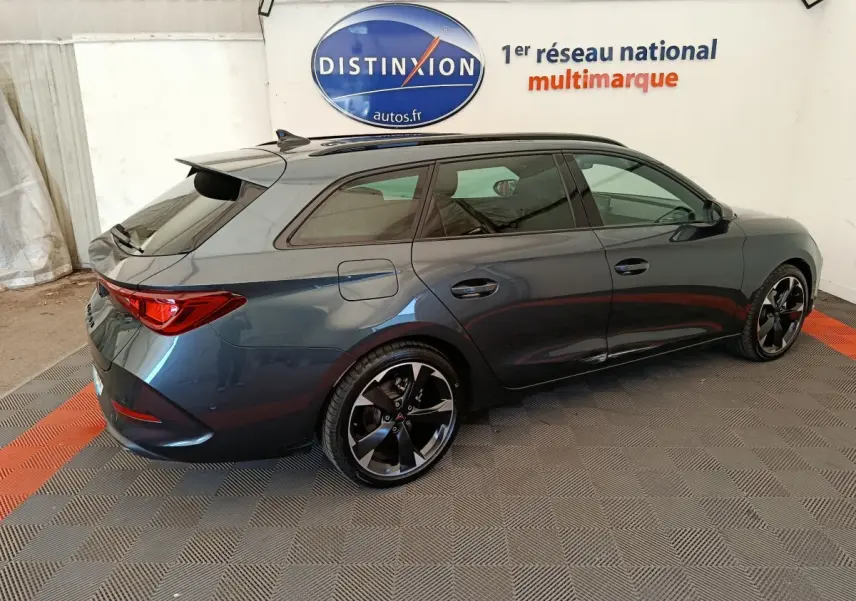 Vue 3/4 arrière droit d'une CUPRA LEON ST 2024 gris foncé avec jantes noires et toit ouvrant en intérieur showroom.