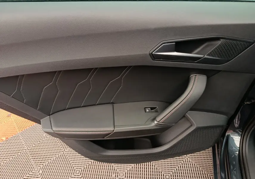 Porte intérieure côté gauche de la CUPRA LEON ST 2024 gris foncé avec surpiqûres rouges et poignée ergonomique.