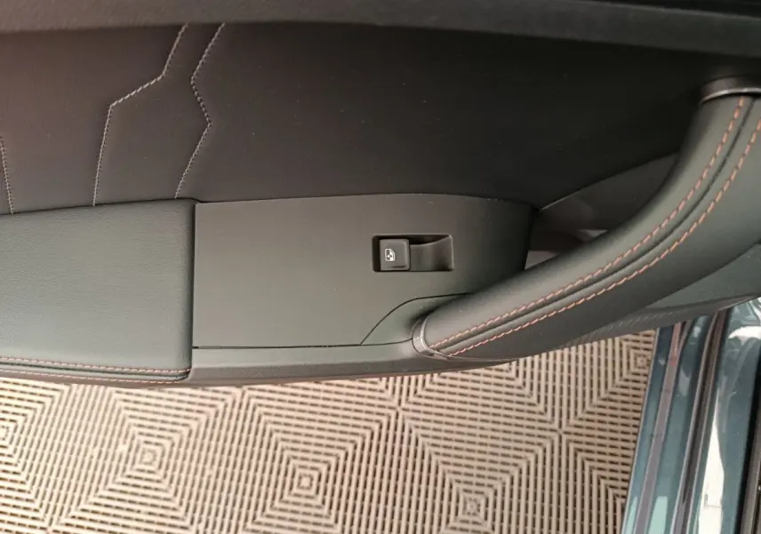 Gros plan sur la poignée intérieure côté gauche de la porte d'une CUPRA LEON ST gris foncé avec surpiqûres orange.