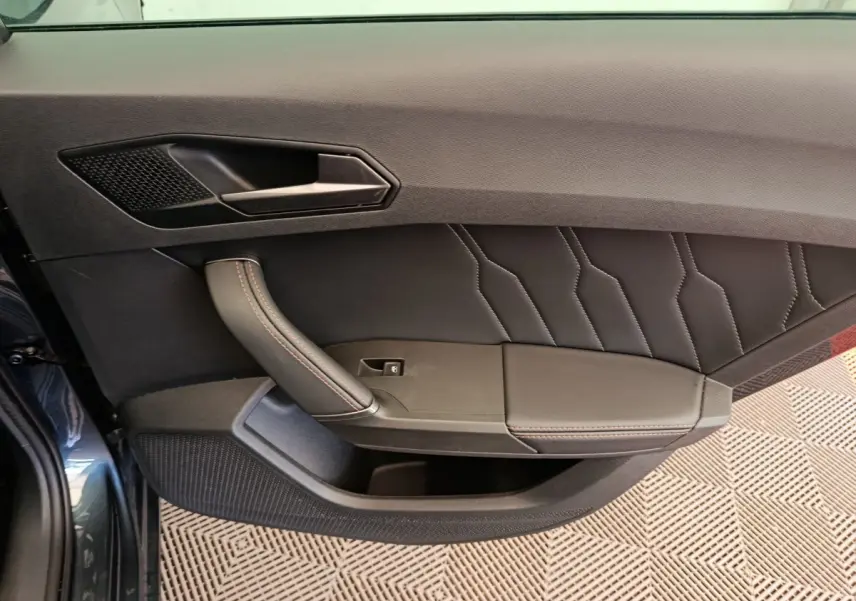 Vue intérieure côté gauche de la porte avant gris foncé de la CUPRA LEON ST avec poignée et surpiqûres rouges.