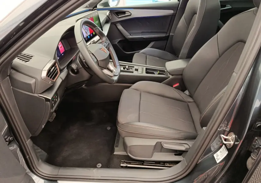 Intérieur côté conducteur de la CUPRA LEON ST gris foncé 2024, avec tableau de bord digital et sièges noirs élégants.