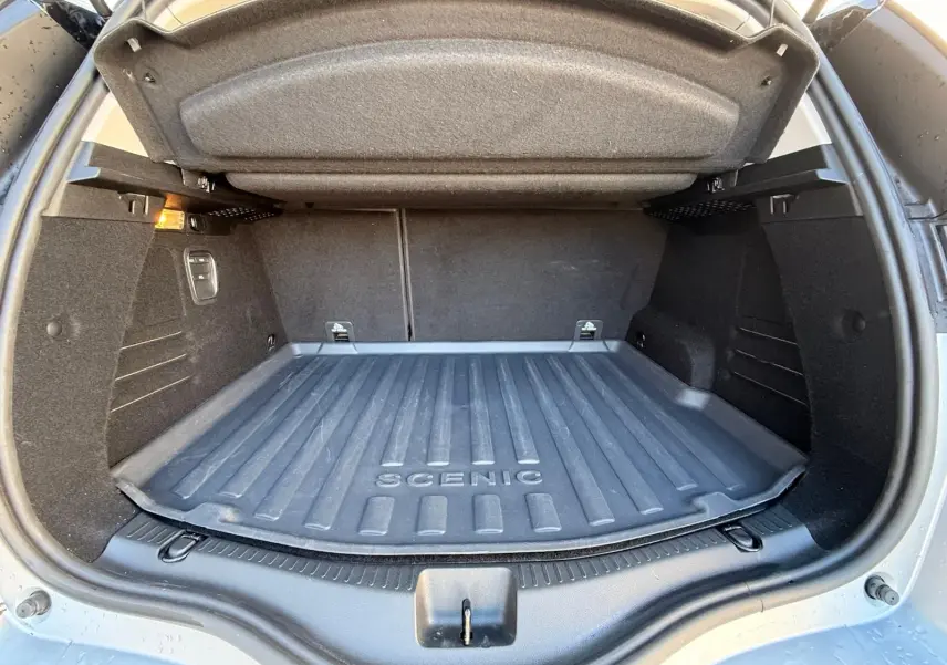 Coffre ouvert en vue arrière d’un Renault Scénic IV gris platine avec tapis de coffre marqué "SCENIC" et toit noir étoile.