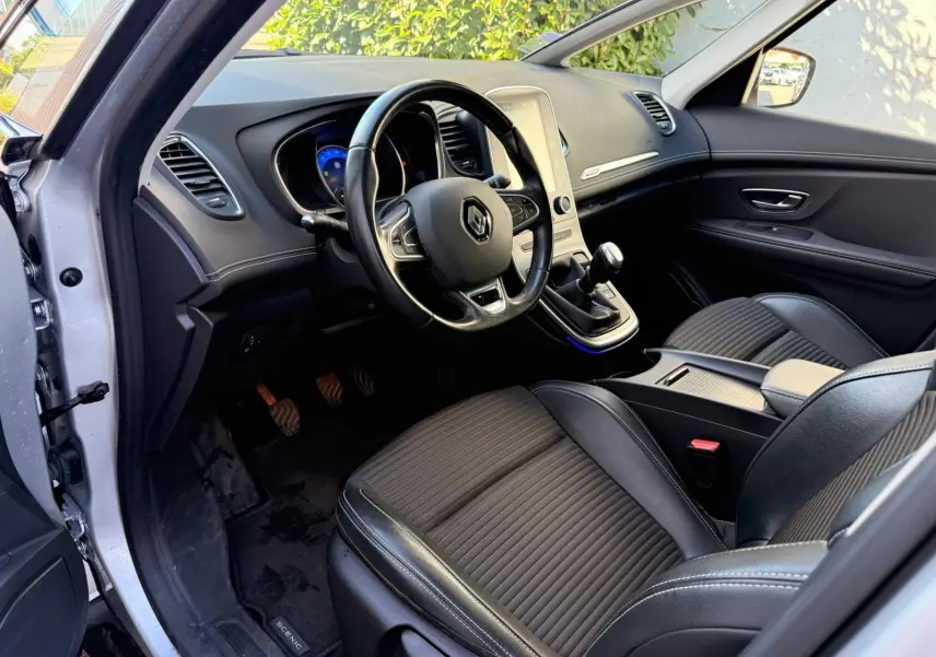 Intérieur avant gauche du Renault Scenic IV 2020 gris platine, volant cuir, tableau de bord moderne et boîte manuelle visible.
