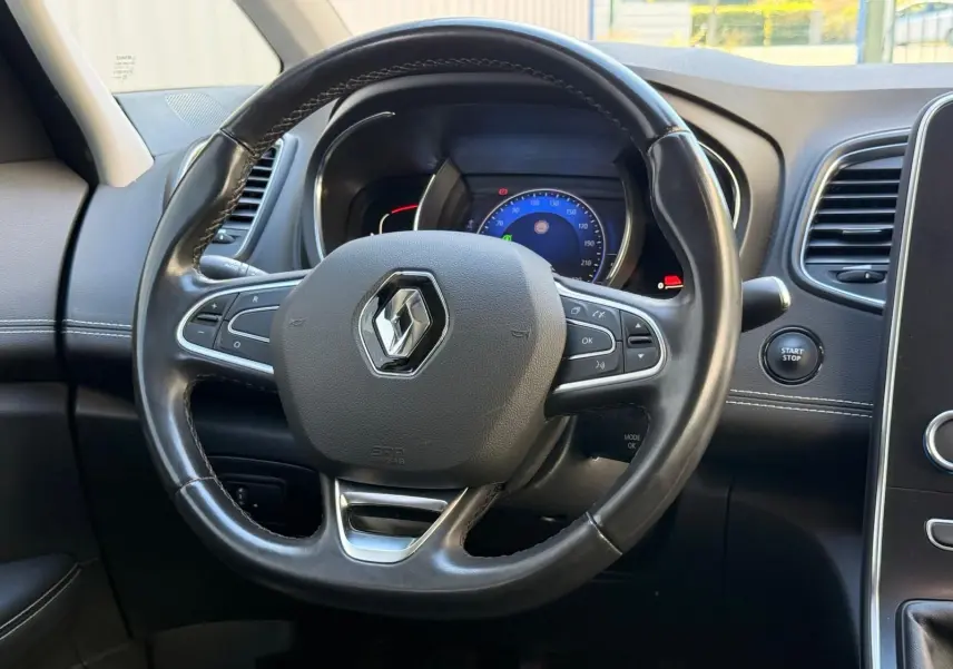 Vue rapprochée du volant noir avec logo Renault et tableau de bord digital du Scenic IV gris platine 2020.