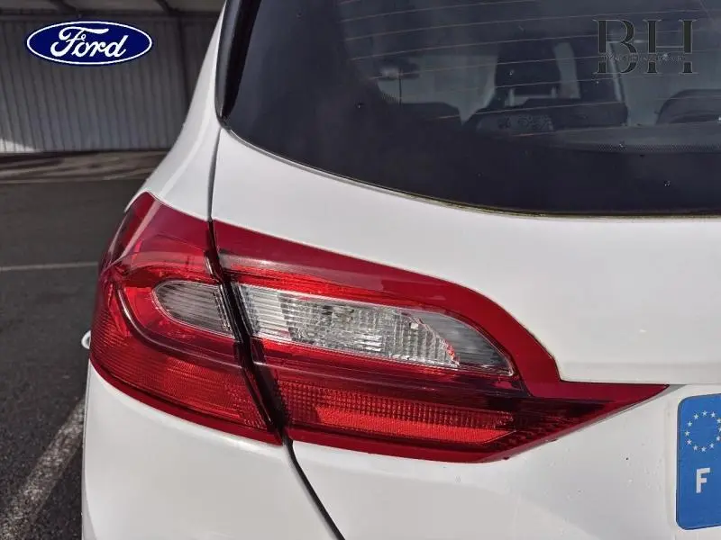 Gros plan sur le feu arrière gauche rouge et blanc d'une Ford Fiesta Blanc Glacier, vue arrière partielle.