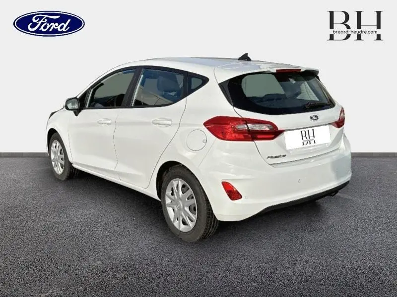 Vue 3/4 arrière droite d'une Ford Fiesta blanche Glacier, avec becquet arrière et feux arrière rouges visibles.