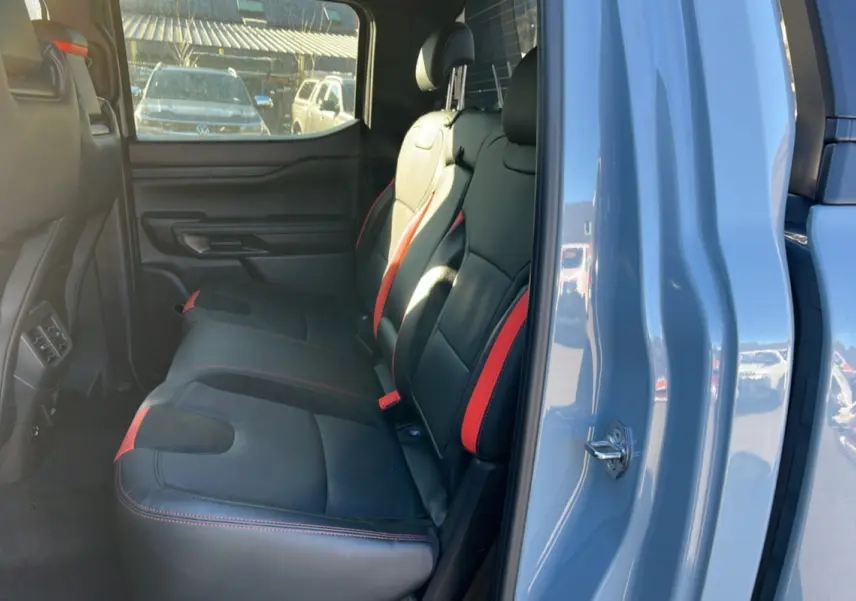 Vue intérieure arrière côté droit du Ford Ranger Raptor 2025, sièges cuir noirs avec surpiqûres rouges, portières gris commandeur.