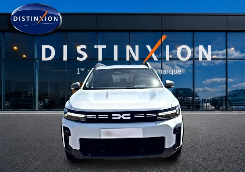 Vue avant d'un Dacia Bigster blanc 2026 avec calandre noire et logo distinctif, devant une vitrine de concession.