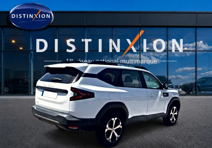 Vue 3/4 arrière droite du SUV blanc Dacia Bigster 2026 avec jantes alu et barres de toit noires.