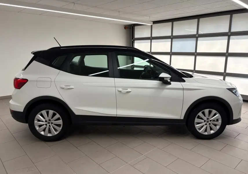 Vue de profil côté gauche du SEAT Arona 2023 blanc avec toit noir, soulignant sa silhouette compacte et ses jantes argentées.