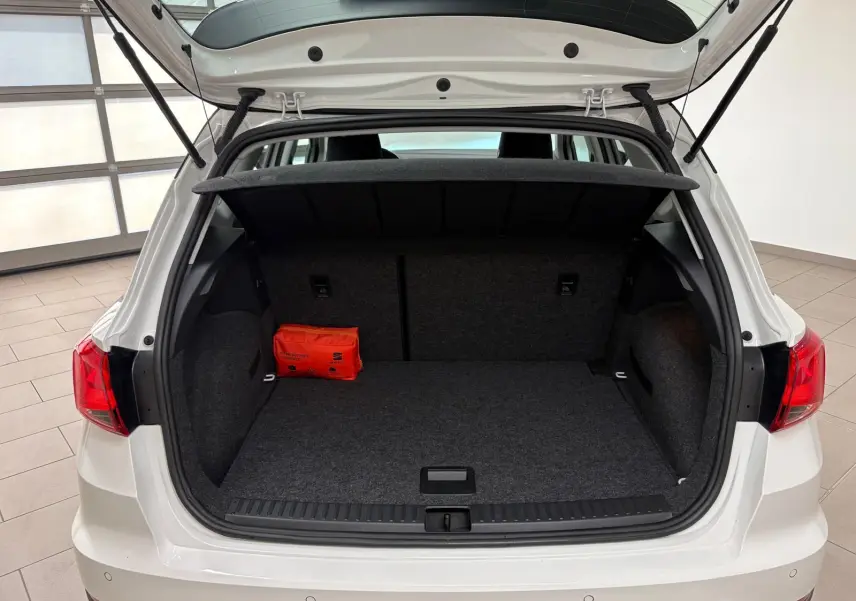 Coffre ouvert vue arrière d'une SEAT Arona blanc toit noir, avec tapis gris et trousse de secours orange à gauche.