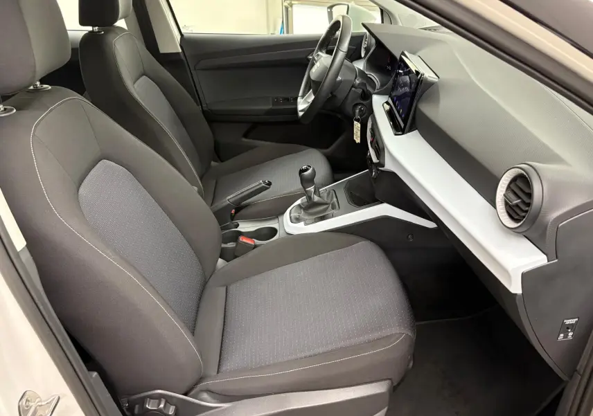 Intérieur avant droit du SEAT Arona 2023 avec sièges gris, tableau de bord blanc et noir, et boîte manuelle visible.