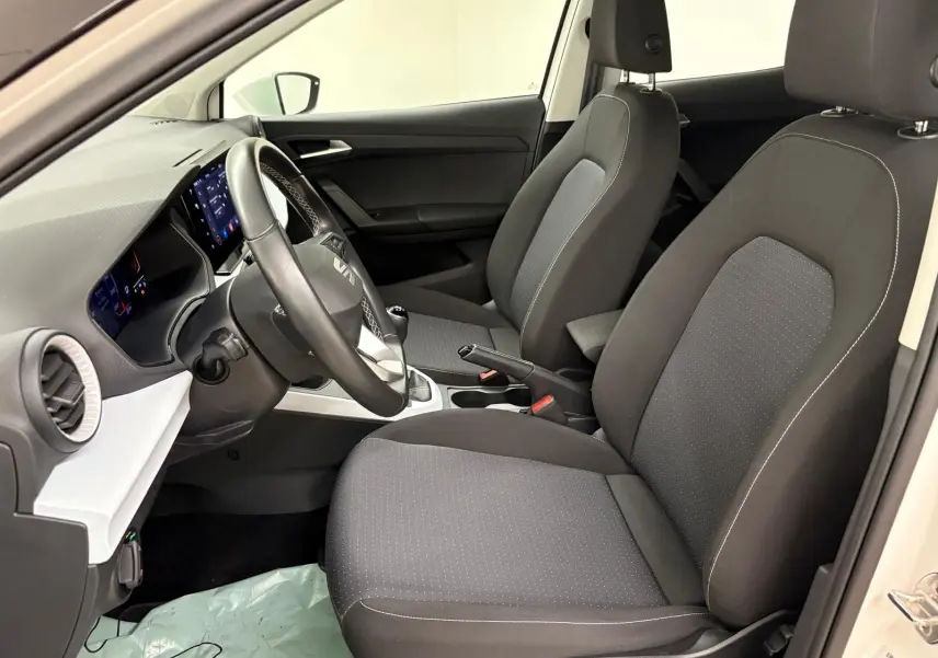 Intérieur avant du SEAT Arona 2023, sièges noirs avec coutures blanches, volant multifonction et tableau de bord moderne.