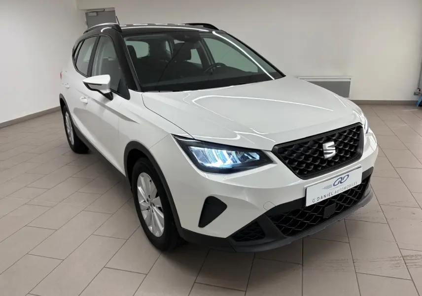 SEAT Arona blanc avec toit noir en 3/4 avant droit, phares allumés et calandre noire distinctive.