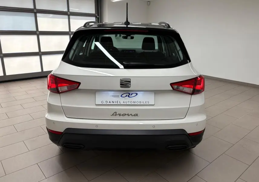 Vue arrière d'un SEAT Arona blanc avec toit noir, dans un showroom lumineux, soulignant ses feux arrière rouges.