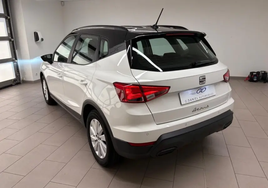 Vue 3/4 arrière droite d'un SEAT Arona blanc avec toit noir, stationné en intérieur sur carrelage gris.