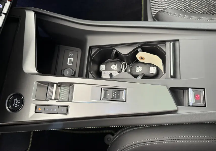 Vue plongeante sur la console centrale grise du Peugeot 308 Hybrid 136 e-DCS6 GT avec boutons de boîte auto et clés dans porte-gobelets.