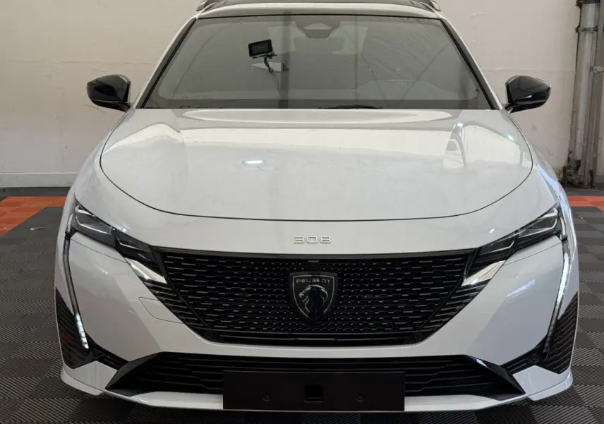 Vue frontale d'une Peugeot 308 Hybrid 136 e-DCS6 GT blanche avec calandre noire et feux LED distinctifs.